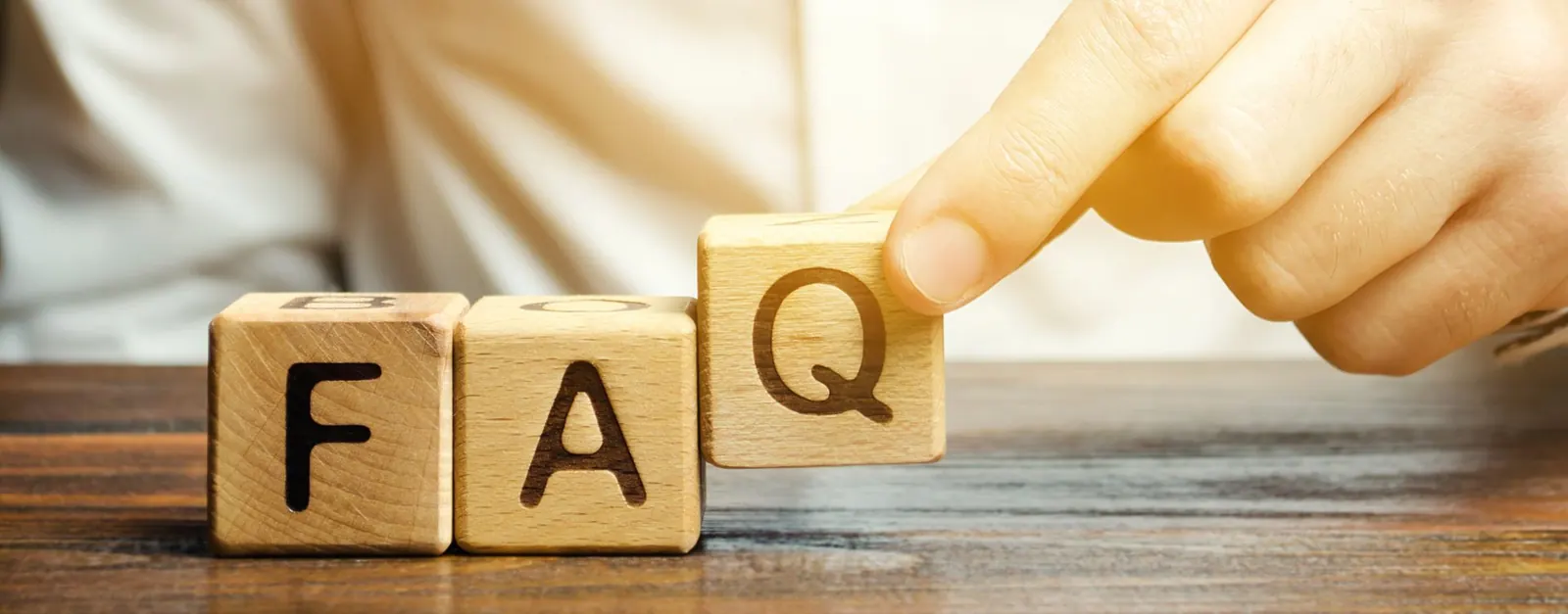 A person is holding a wooden block with the word FAQ written on it.